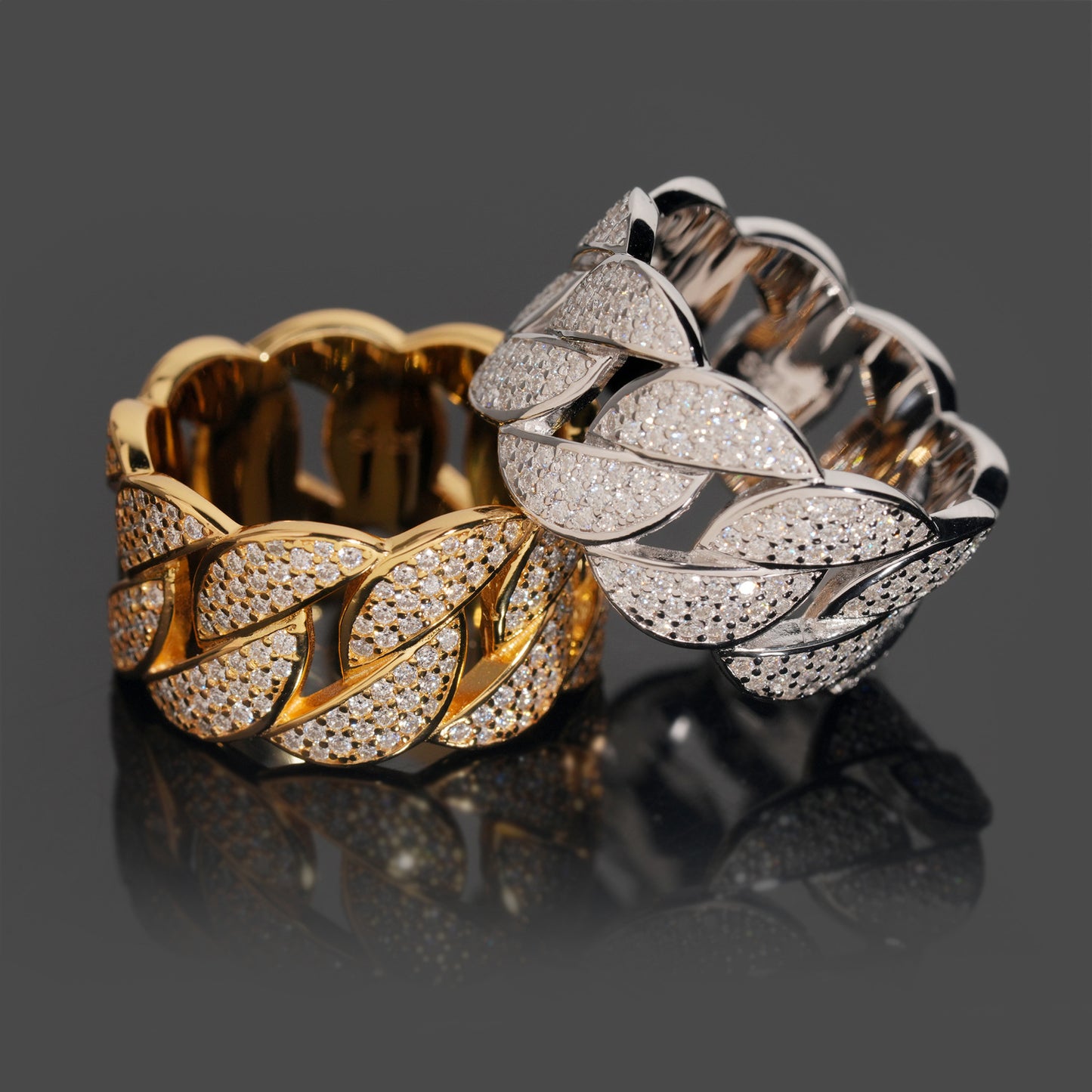 Two gold and silver leaf-patterned rings on a reflective surface with a dark background