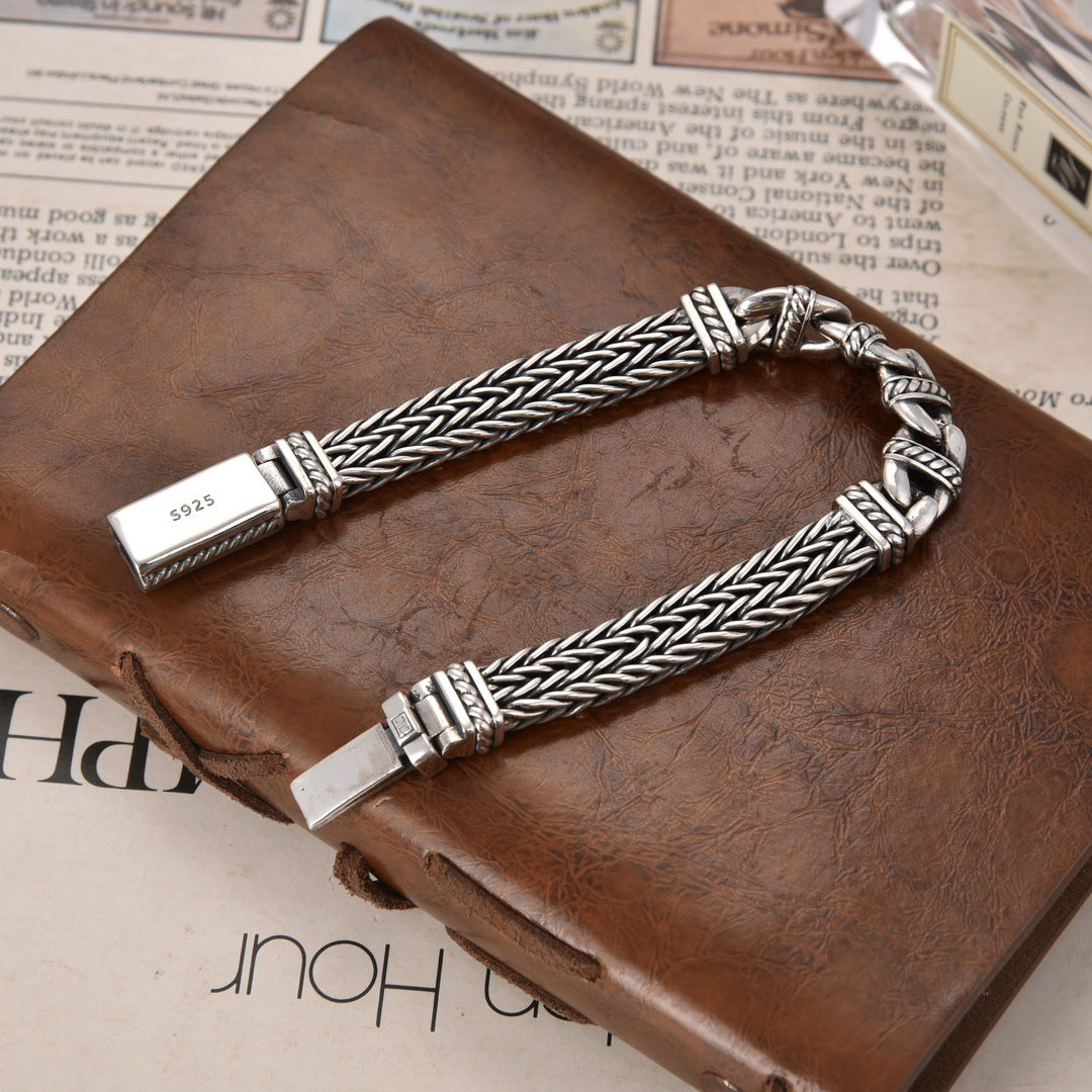 Silver braided bracelet on a brown leather surface with newspaper in the background