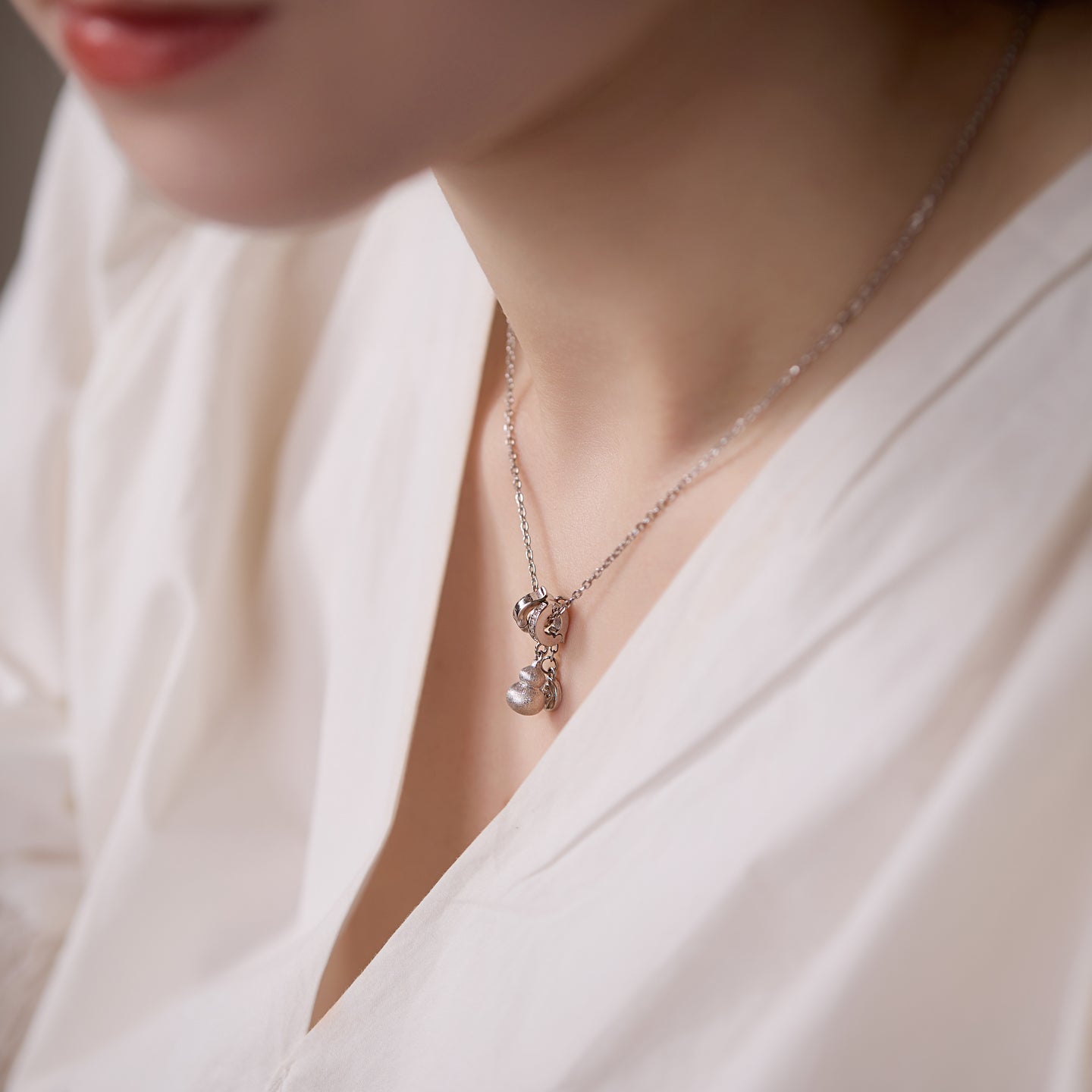 Close-up of a silver necklace with a pendant on a person wearing a white top.