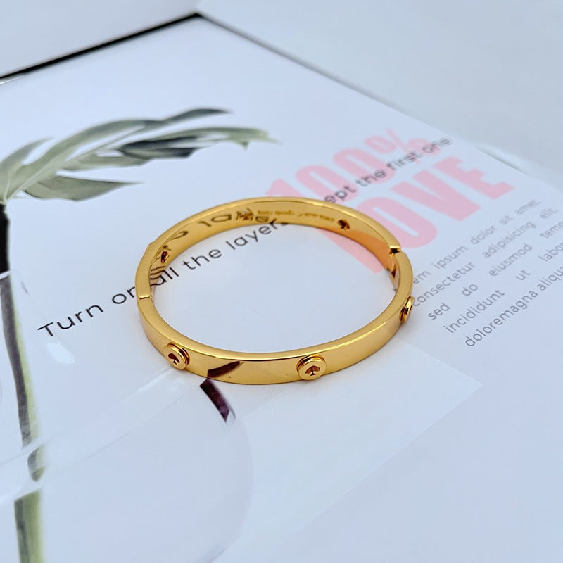 Bangle on a soft velvet or marble surface, showcasing the hollow heart detail and gold luster. Alt: “Kate Spade Elegant 18K Gold Heart Bangle Bracelet – Hollow Love Heart Design.”