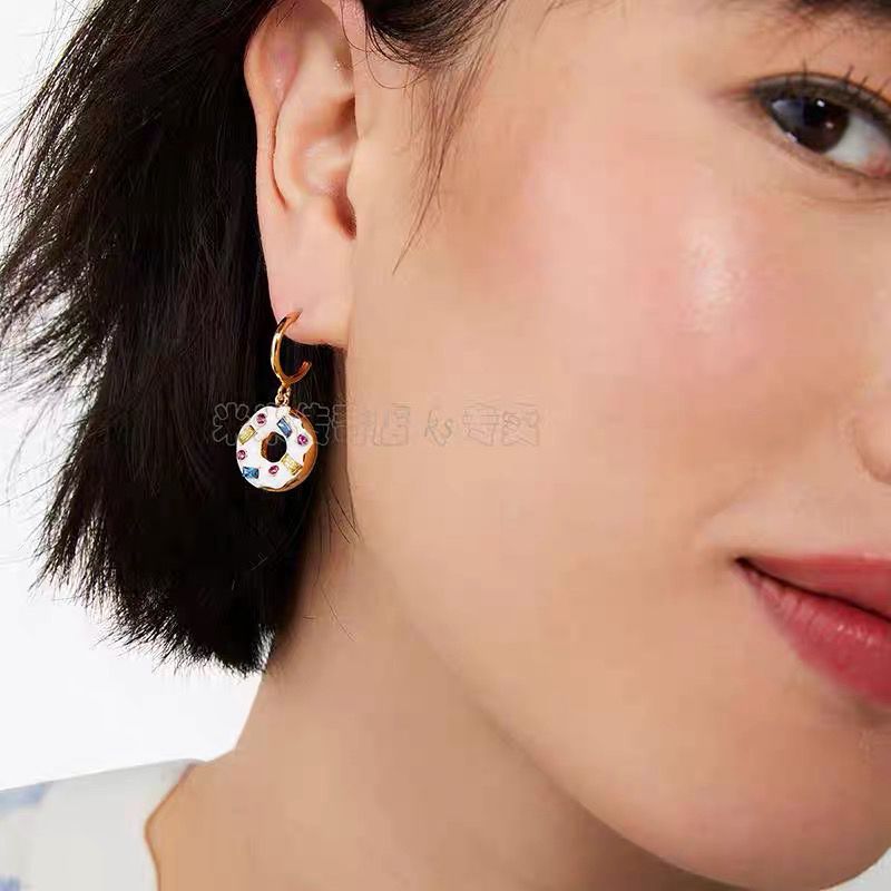 Earrings on a soft pastel pink or cream background, showcasing the donut and coffee charms dangling from huggie hoops. Alt: “Kate Spade Coffee Break Donut Huggies – Enamel Food Jewelry.”