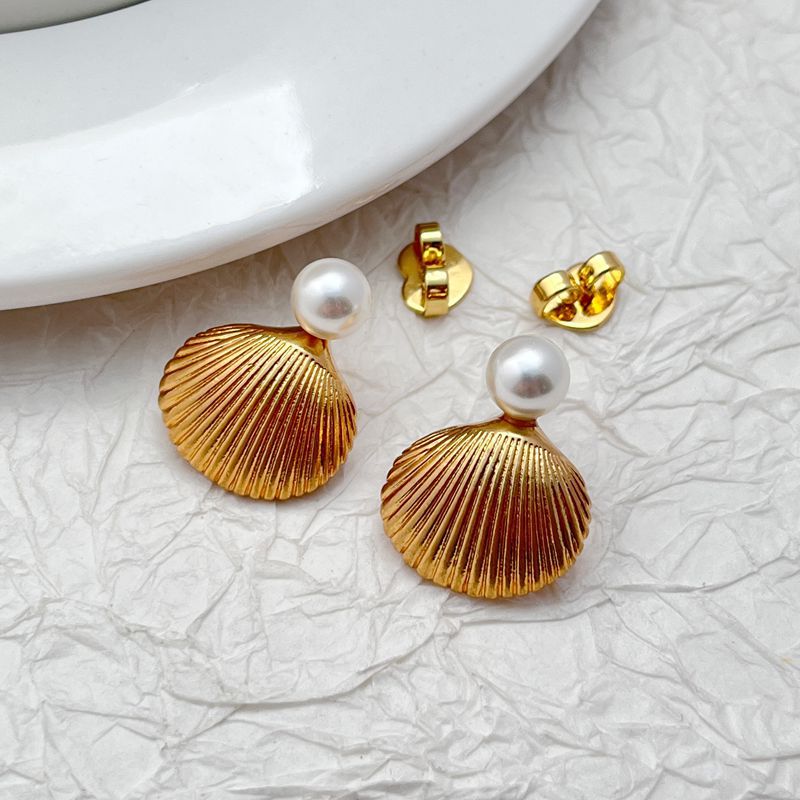 Earrings on a soft sand-beige or seafoam green background, showcasing the sculpted gold shell with pearl or crystal center. Alt: “Kate Spade Reef Treasure Shell Stud Earrings – Gold Seashell Nautical Jewelry.”