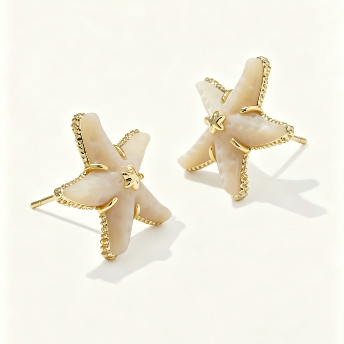 A pair of starfish-shaped earrings with cream-colored shell inlays and gold-tone metal borders, displayed on a clean off-white background.