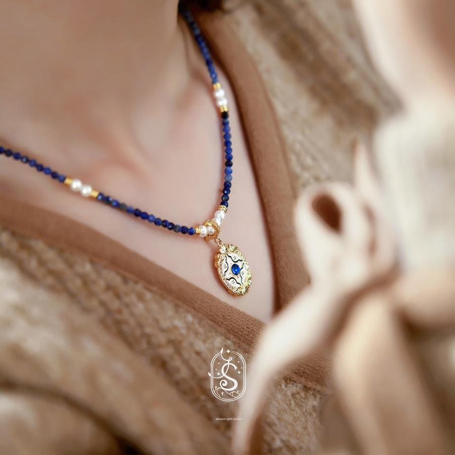 Necklace with blue beads and a decorative pendant worn by a person, with a blurred background.