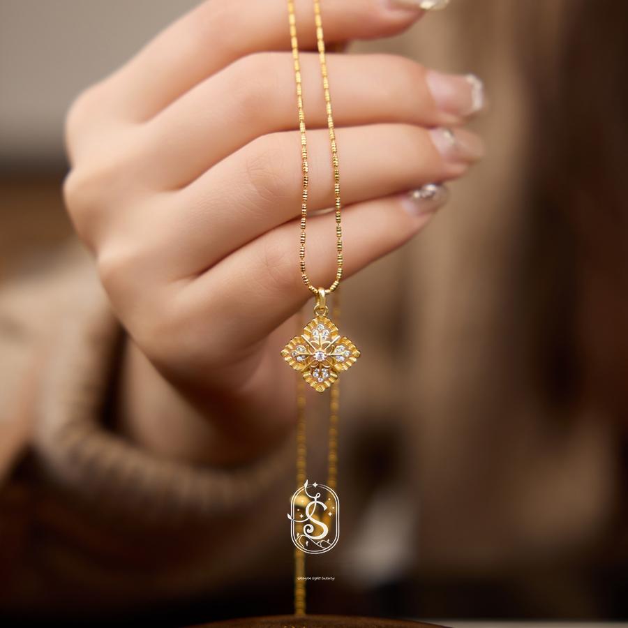 Gold necklace with a diamond pendant held by a hand against a blurred background