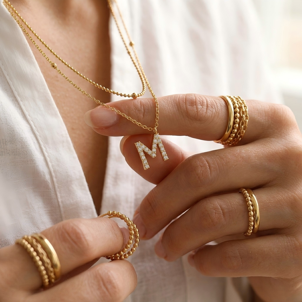 Include close-up shots showing the double "M" pendants at different lengths against the collarbone and wider shots showing the complete layered look.