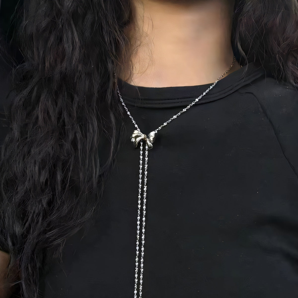 Person wearing a black garment with a silver necklace featuring a butterfly pendant.