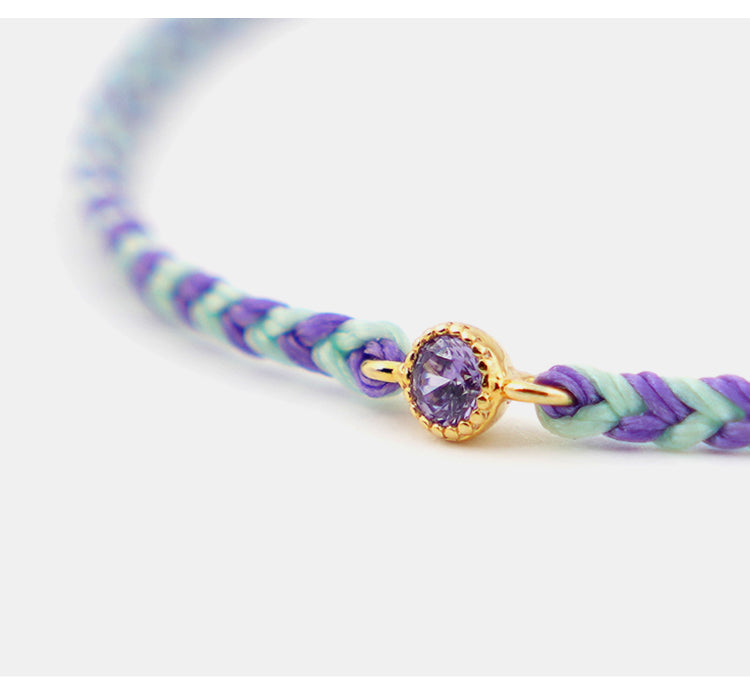 Bracelet with purple and green braided design and a gold clasp with a purple gemstone on a white background.