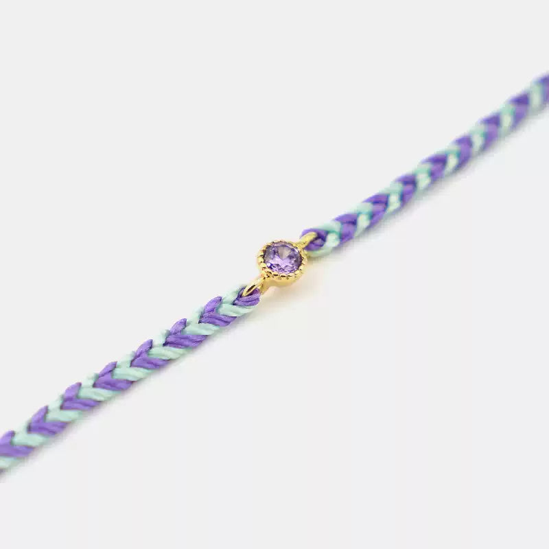 Bracelet with purple and green braided design and a purple gemstone on a white background