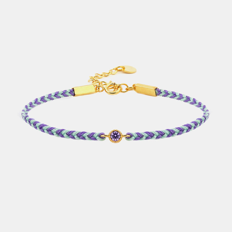 Braided bracelet with purple and green pattern and gold clasp on a white background