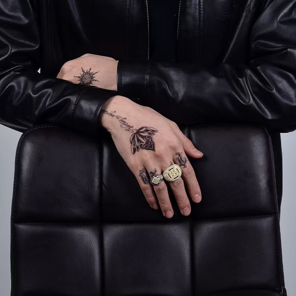 Person wearing a black leather jacket with visible tattoos on their hands and fingers.