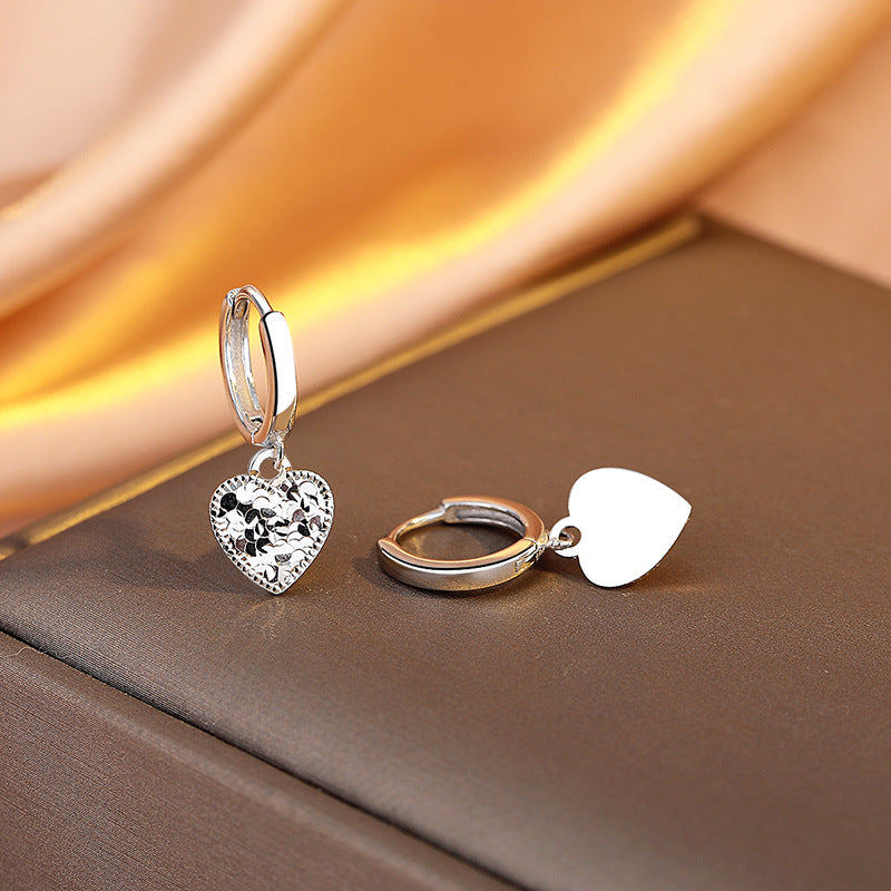 Heart-shaped silver earrings on a brown fabric background