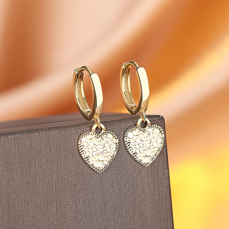 Gold hoop earrings with heart-shaped pendants on a gray surface with a gradient background