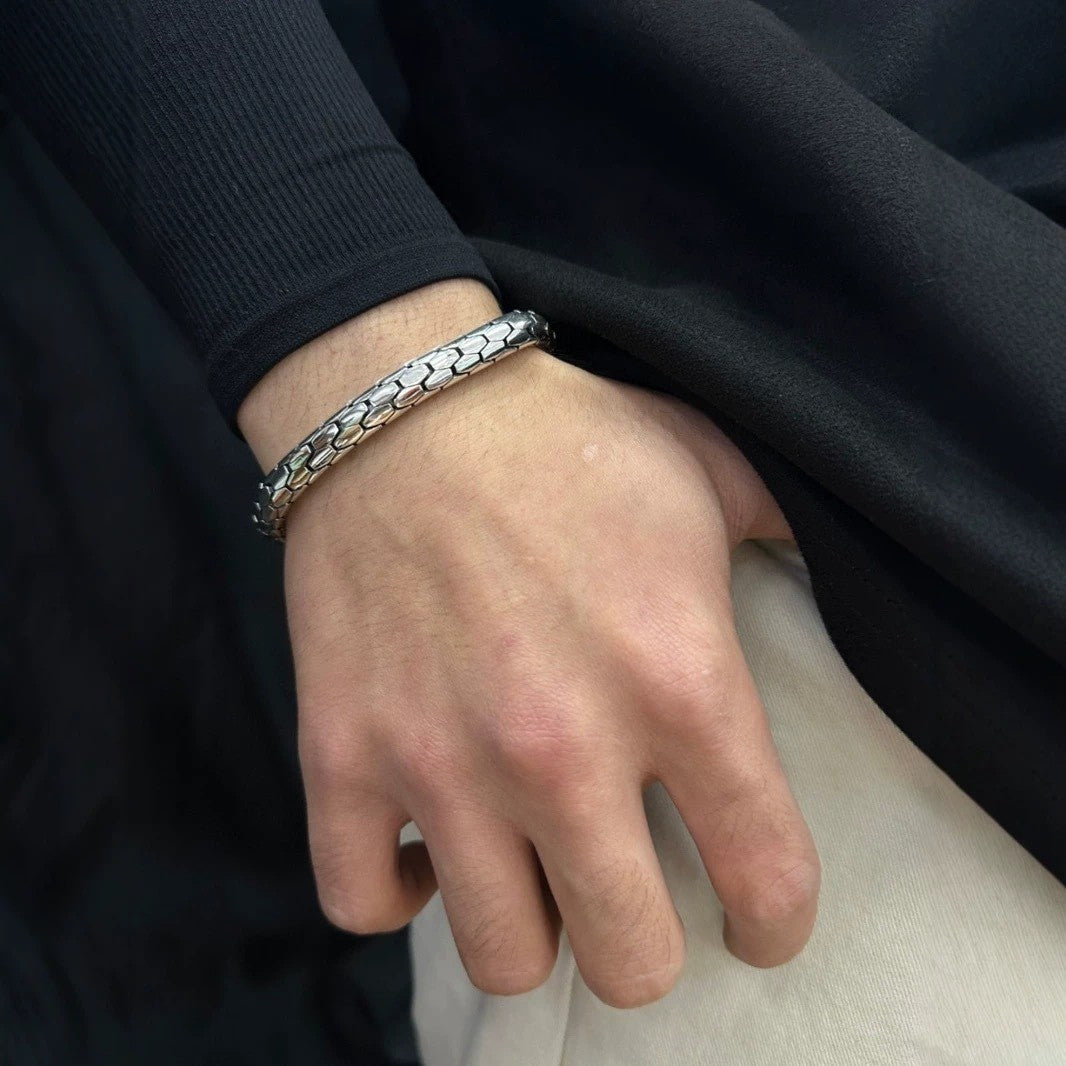 Hand wearing a silver bracelet with a dark background