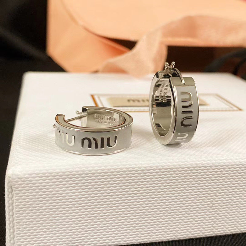 Clean, shadowless studio shot on a white or light grey background, showcasing the earrings' full sculptural form and rich gold-tone finish. Alt text: "Miu Miu Brass Designer Earrings in Gold-Tone - Architectural Statement Piece."