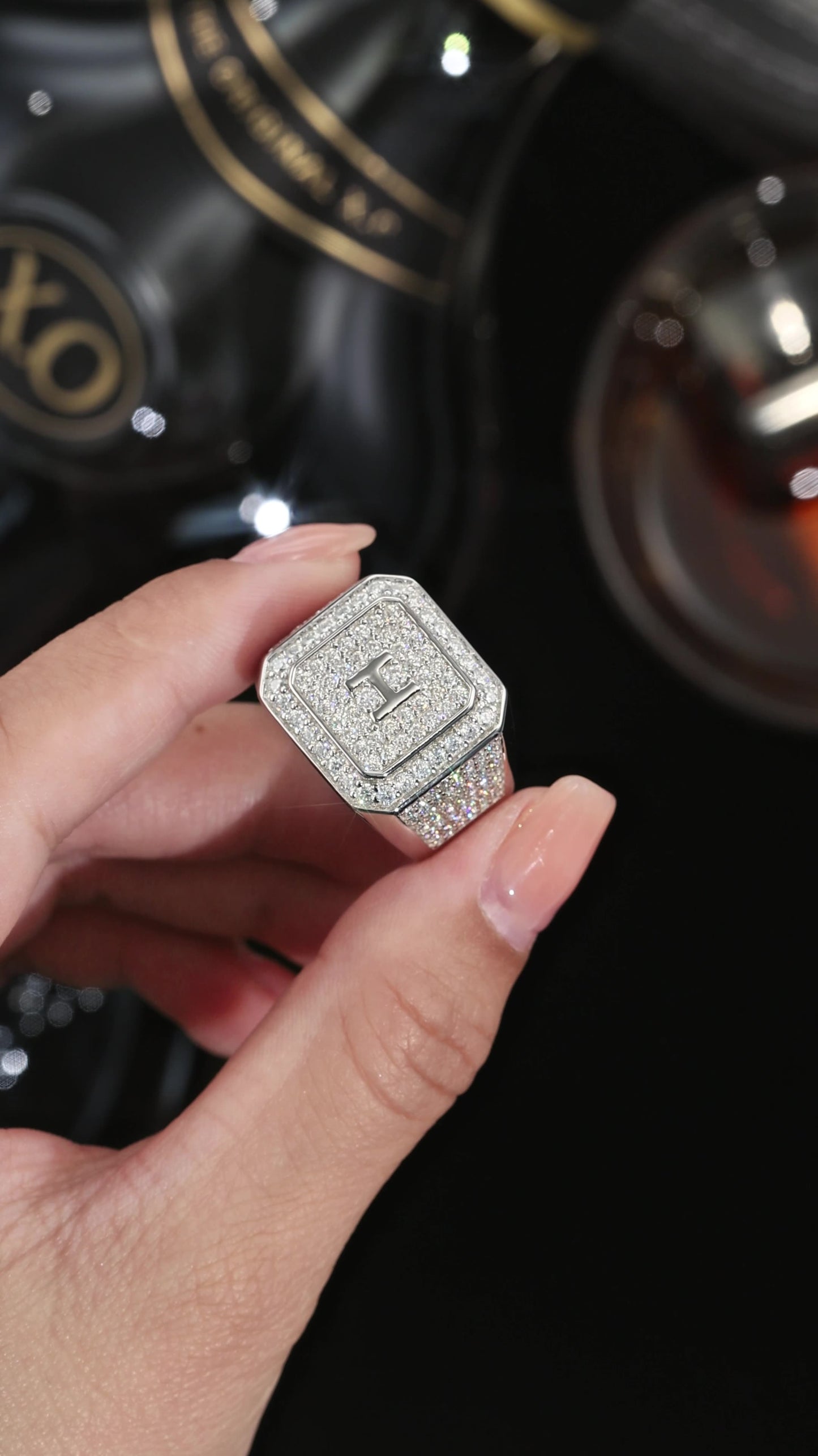 Silver ring with gemstones held by a hand against a dark background