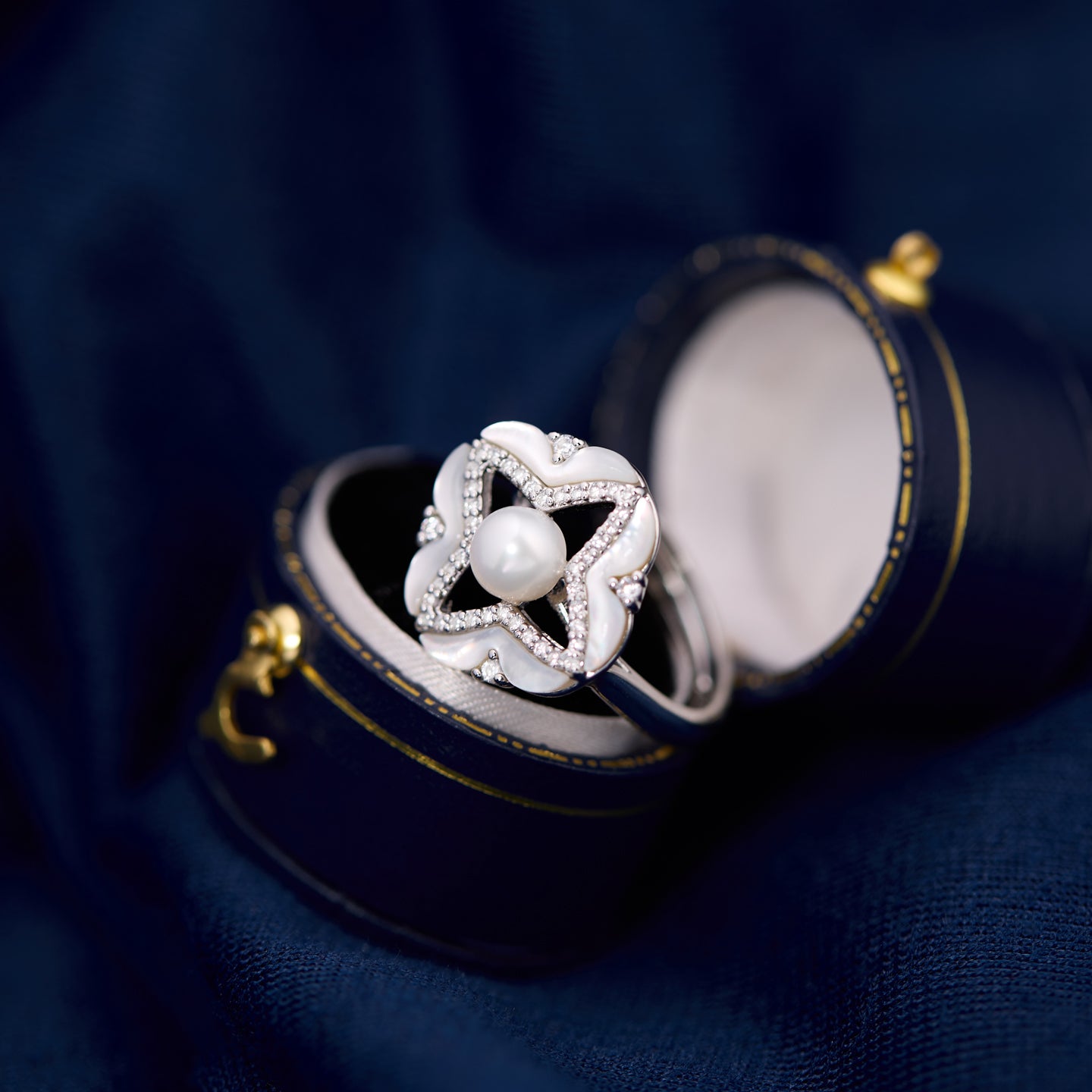 Silver ring with a pearl in a jewelry box on a dark blue fabric background