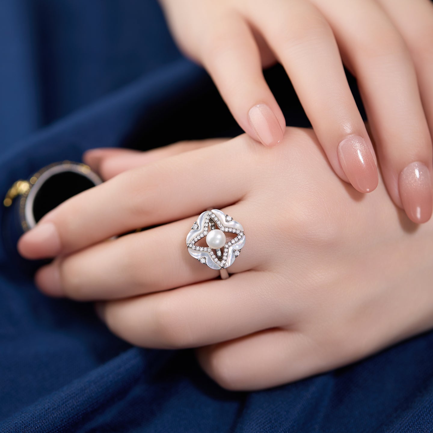Silver ring with a pearl on a hand against a blue fabric background