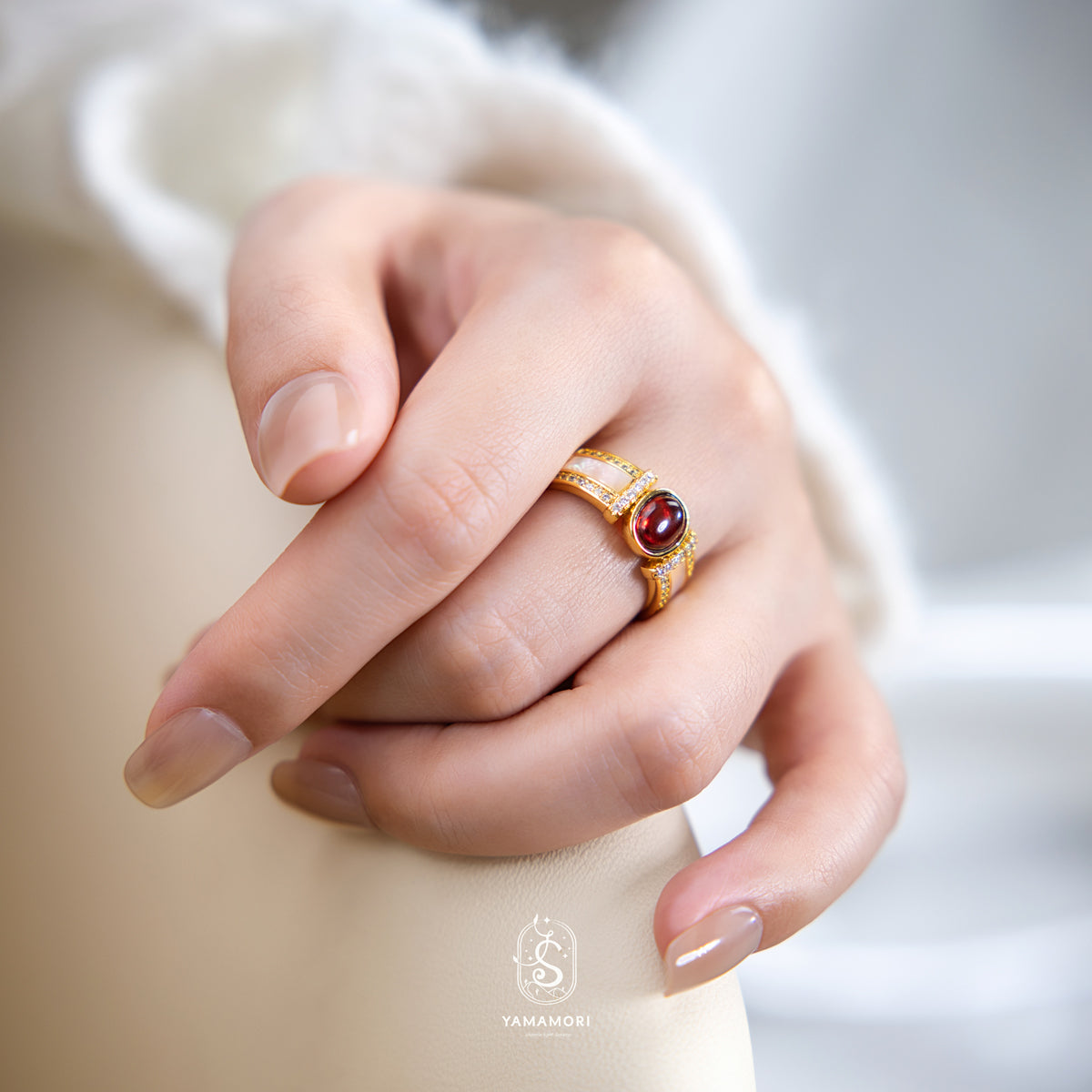 Close-up of a hand wearing a gold ring with a red gemstone, brand 'YAMAMORI' visible.