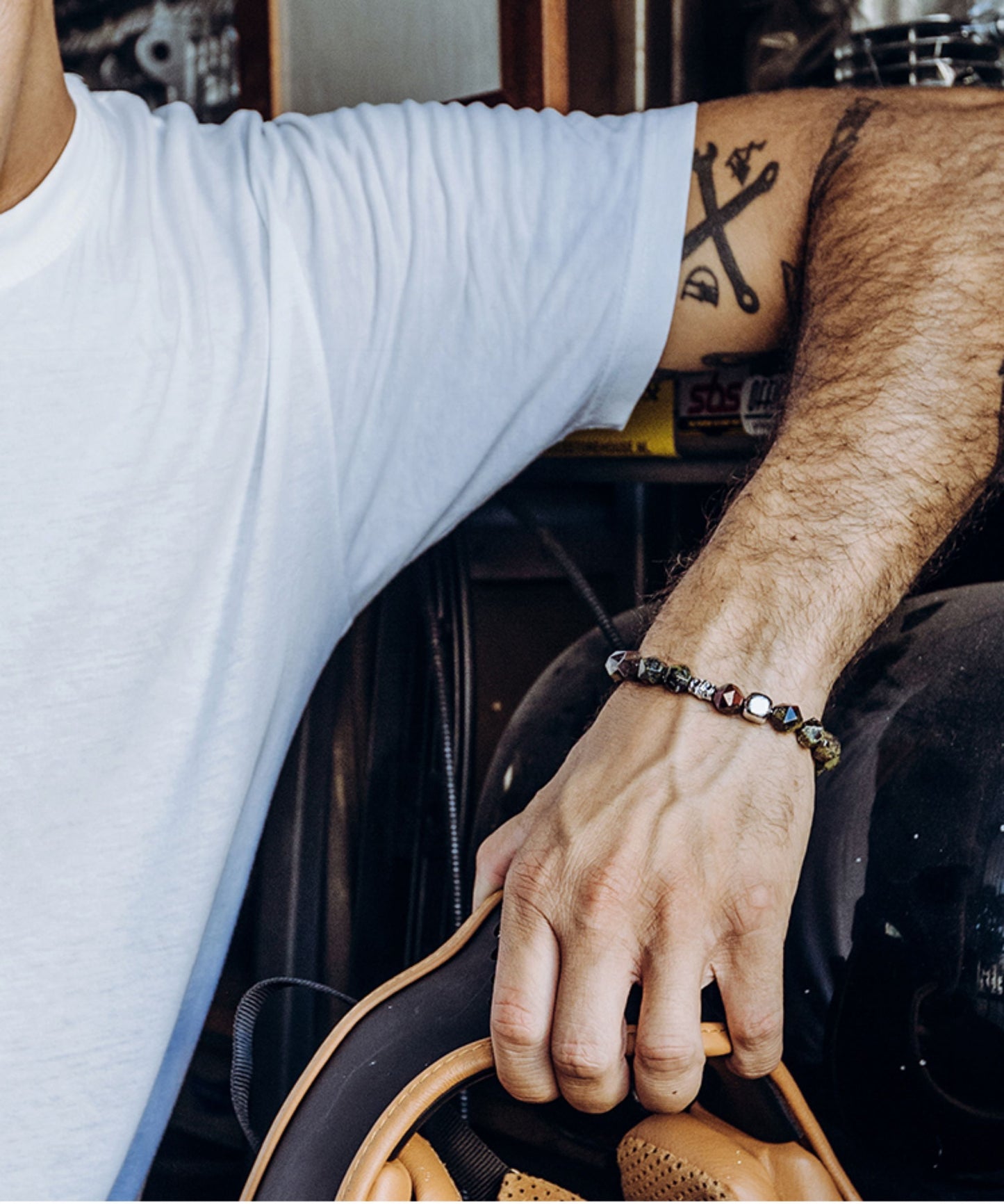 Person holding a steering wheel with tattoos on arm and wearing a bracelet.
