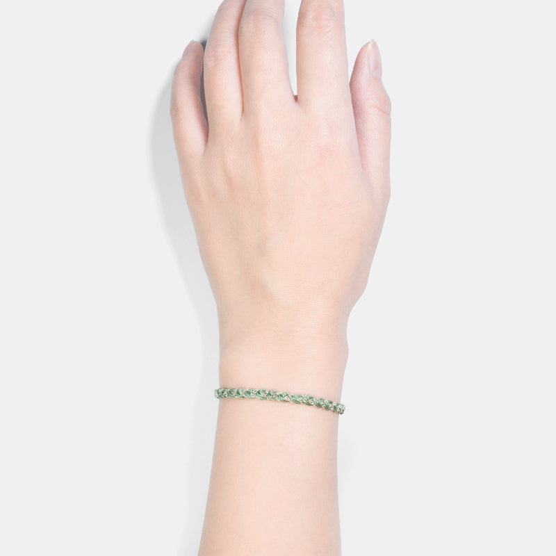 Hand wearing a green bracelet on a light gray background