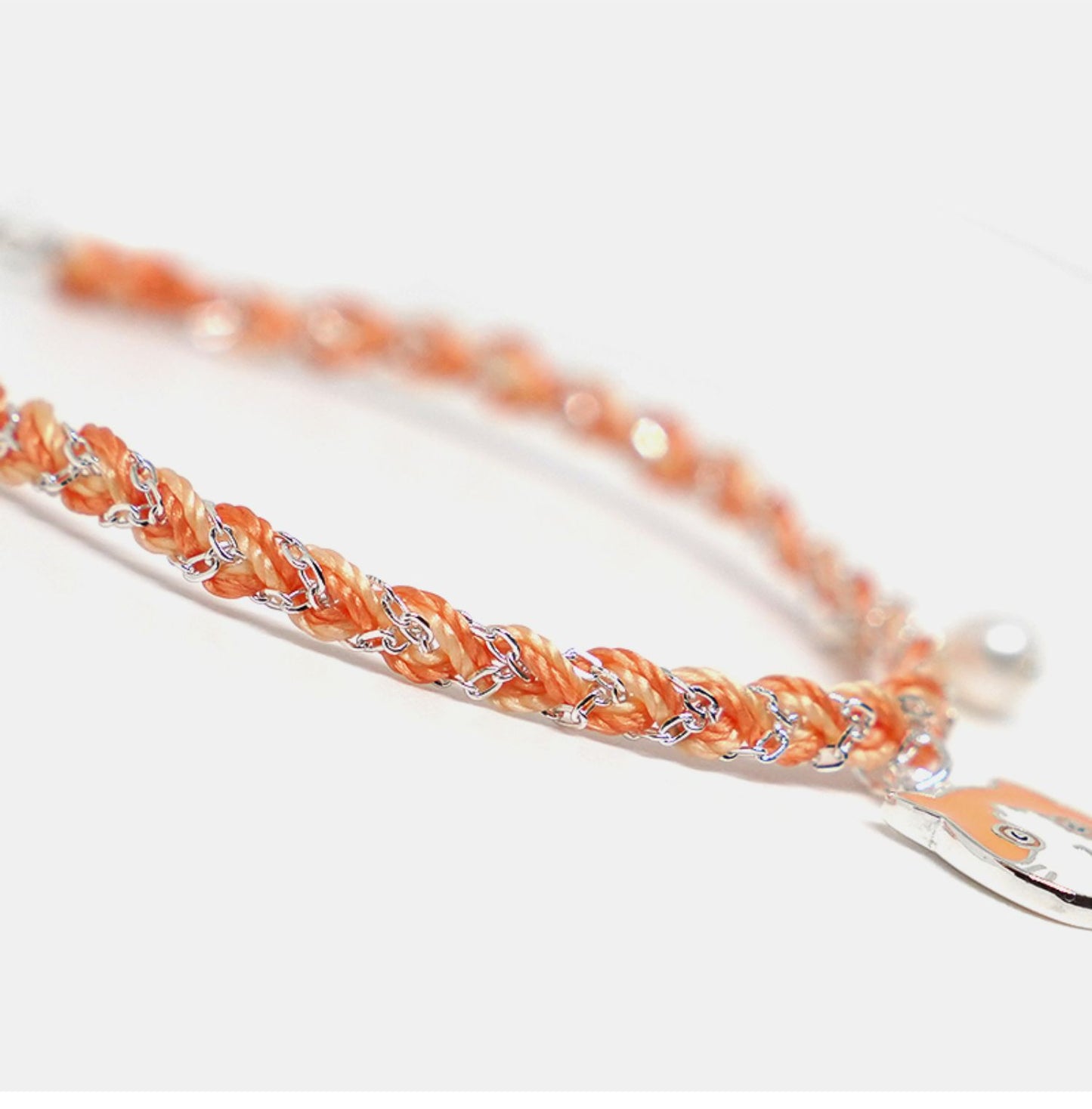 Close-up of a braided orange bracelet with silver accents on a white background