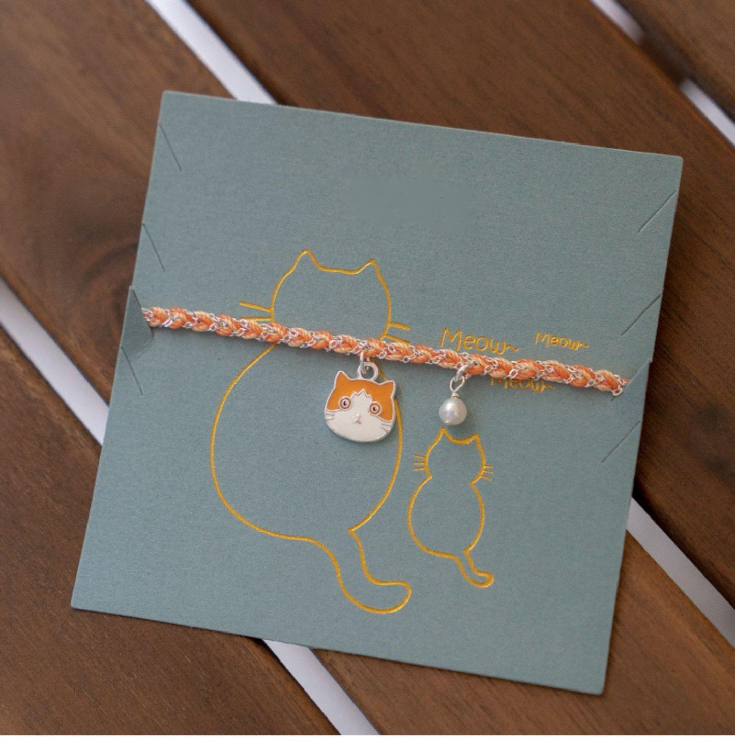 Cat-themed bracelet on a matching card with cat illustrations on a wooden surface