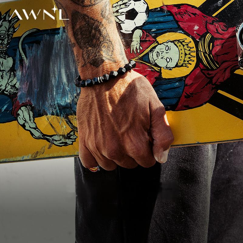 Person holding a colorful skateboard with tattoos and a bracelet against a blurred background