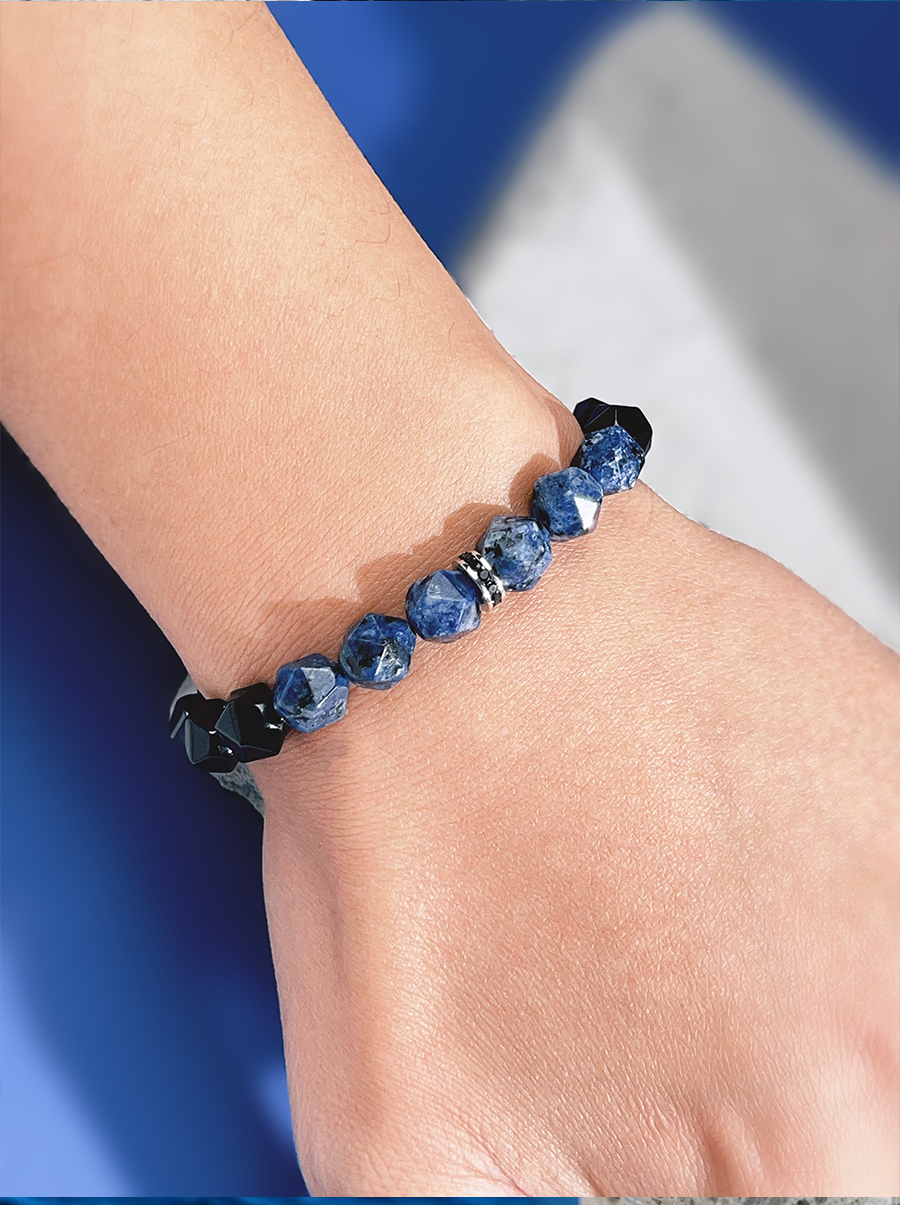 Close-up of a wrist wearing a blue beaded bracelet against a blue and gray background