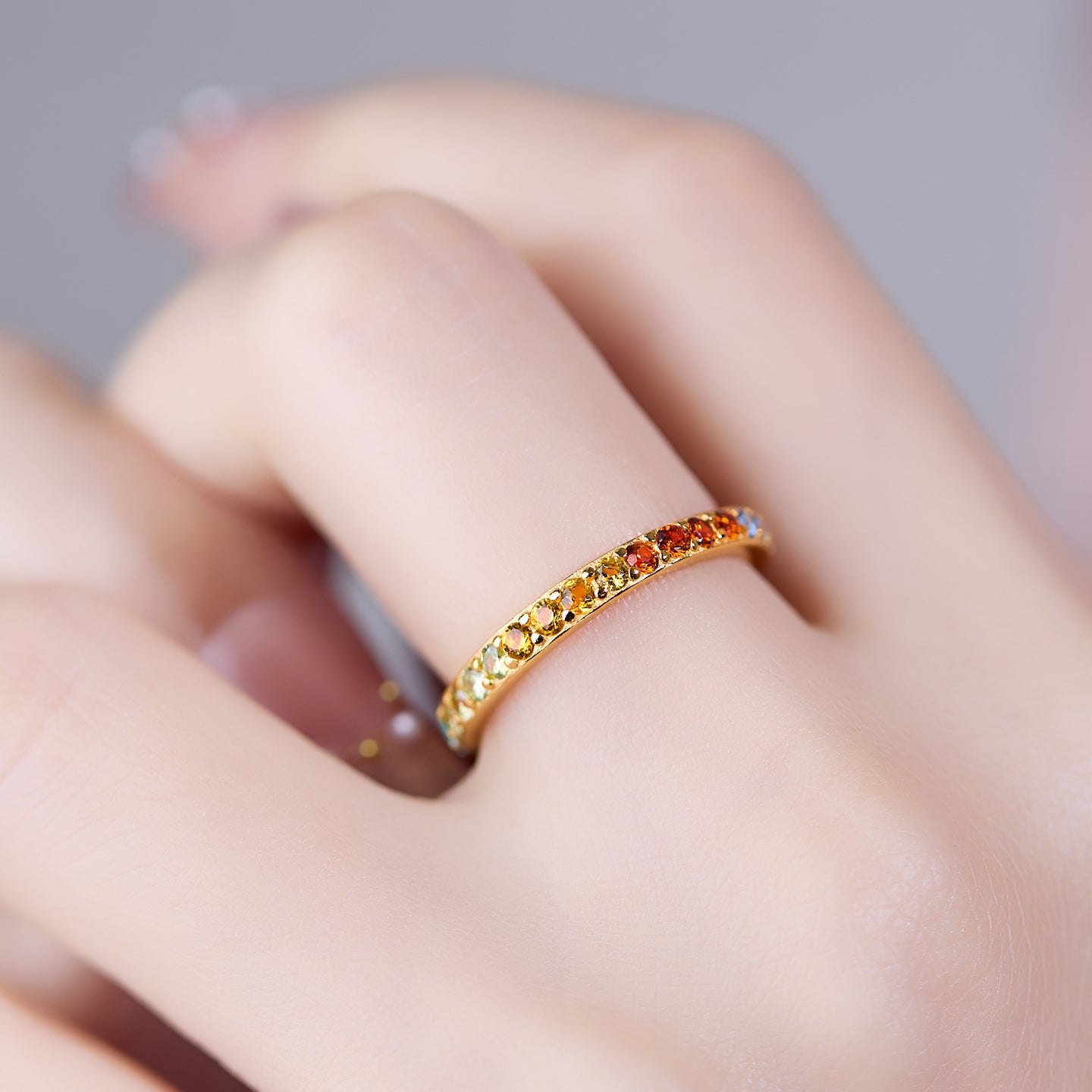 Gold ring with colorful stones on a finger against a neutral background