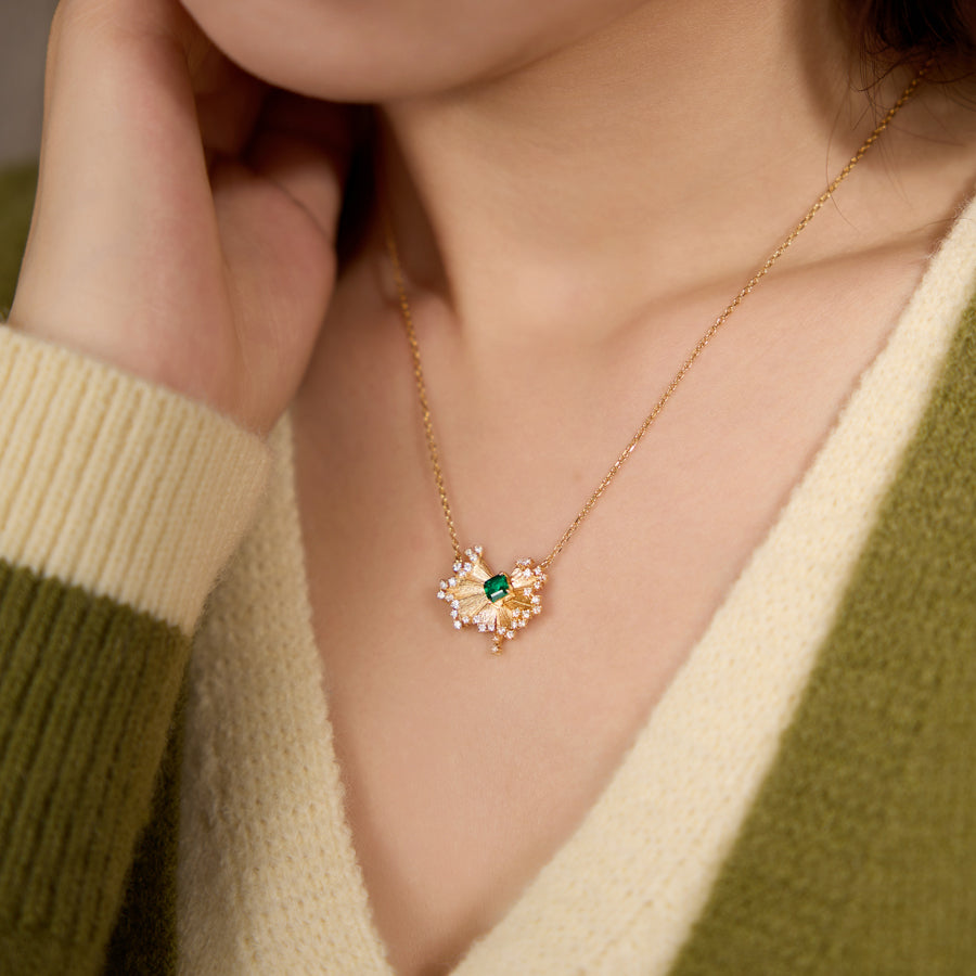 Gold necklace with a green gemstone worn by a person in a green sweater.
