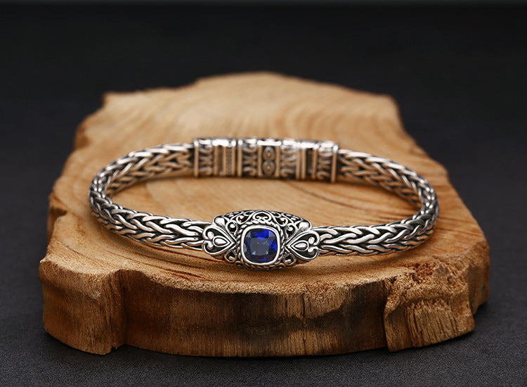Silver bracelet with a blue gemstone on a wooden block against a dark background