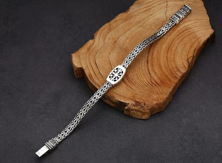 Silver bracelet with intricate design on a wooden block against a dark background