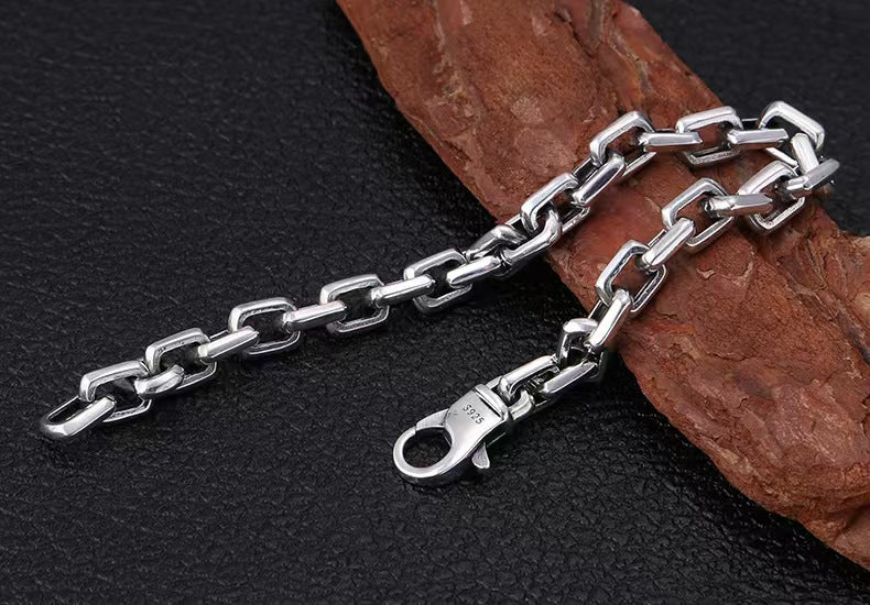 Silver chain necklace on a dark surface with a wooden piece