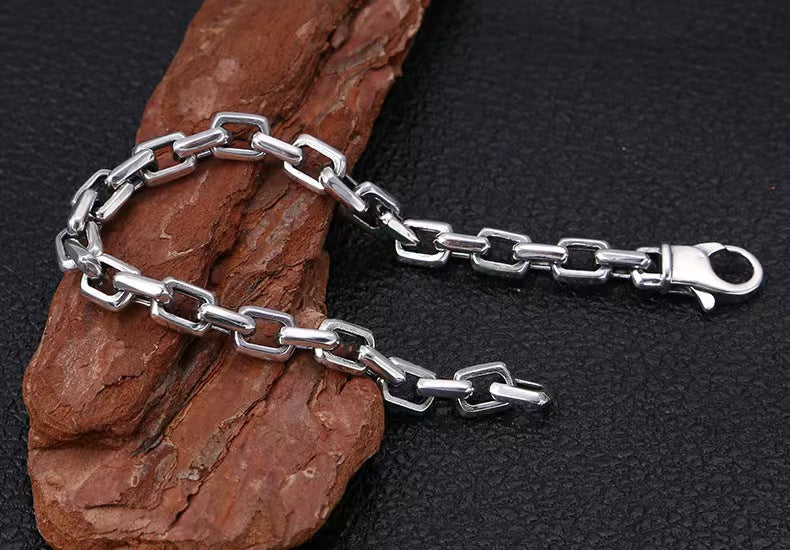 Silver chain bracelet on a textured brown rock against a black background