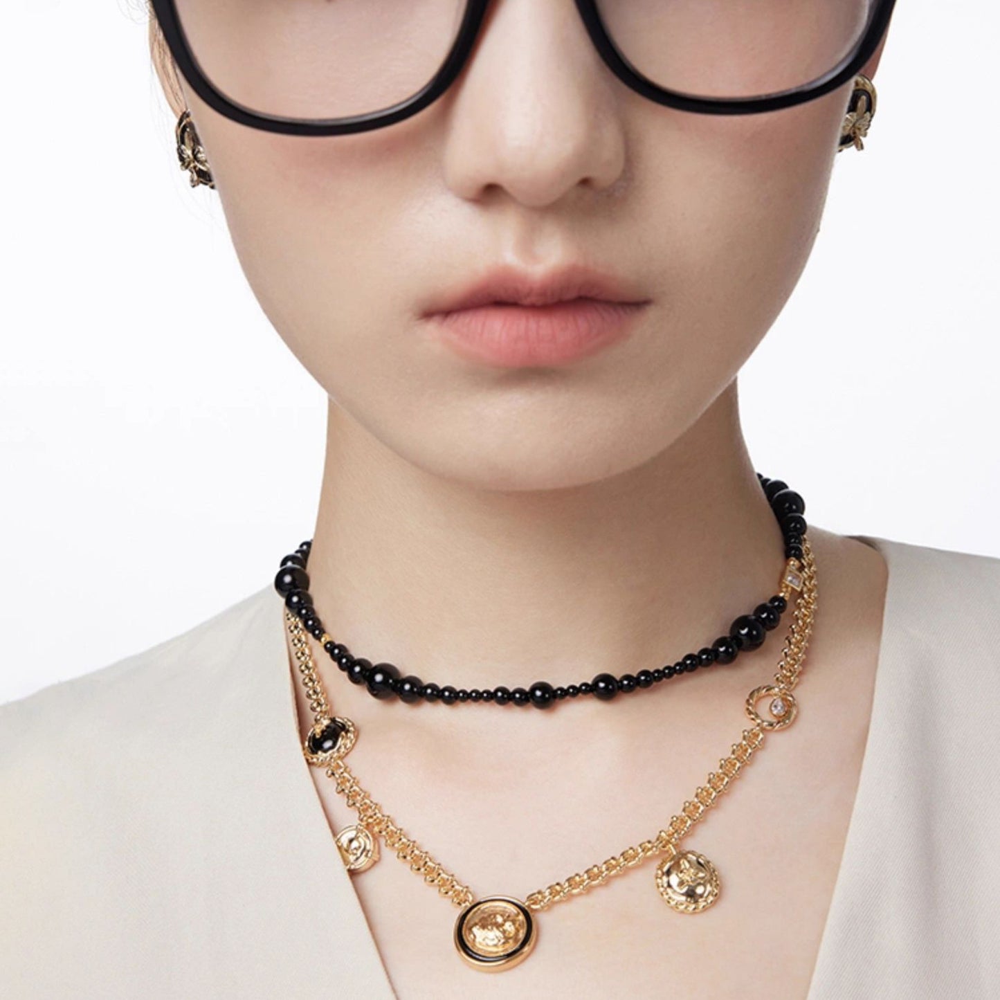 Person wearing a gold necklace with black beads on a plain background