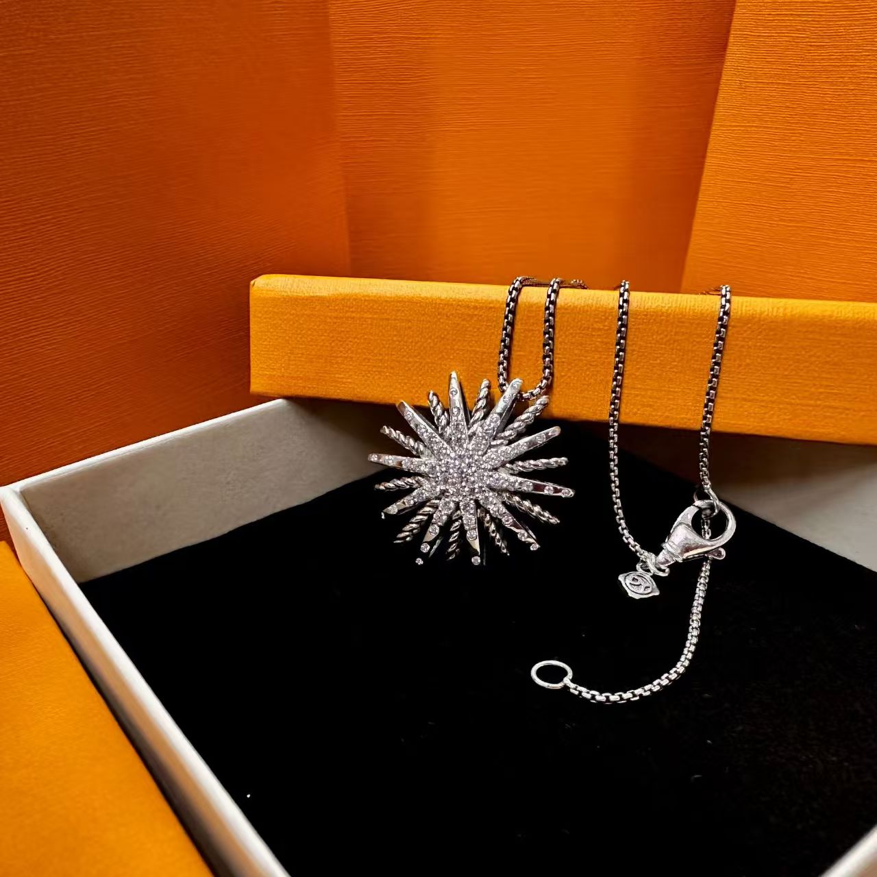 Two silver necklaces on a black tray with an orange background