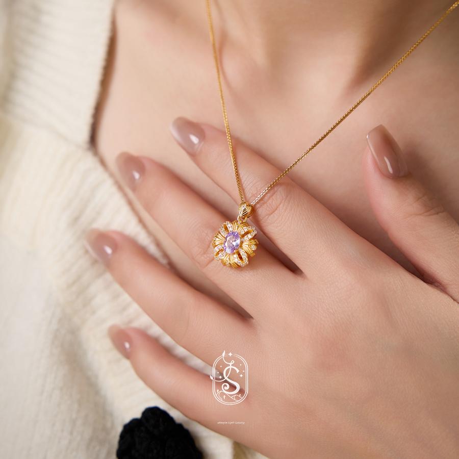Gold necklace with a purple gemstone held by a hand against a neutral background