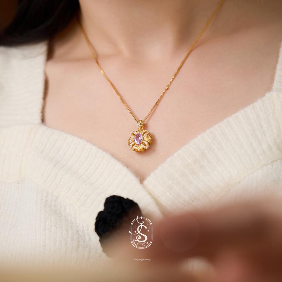 Gold necklace with a pendant worn by a person in a white sweater, with a blurred background.