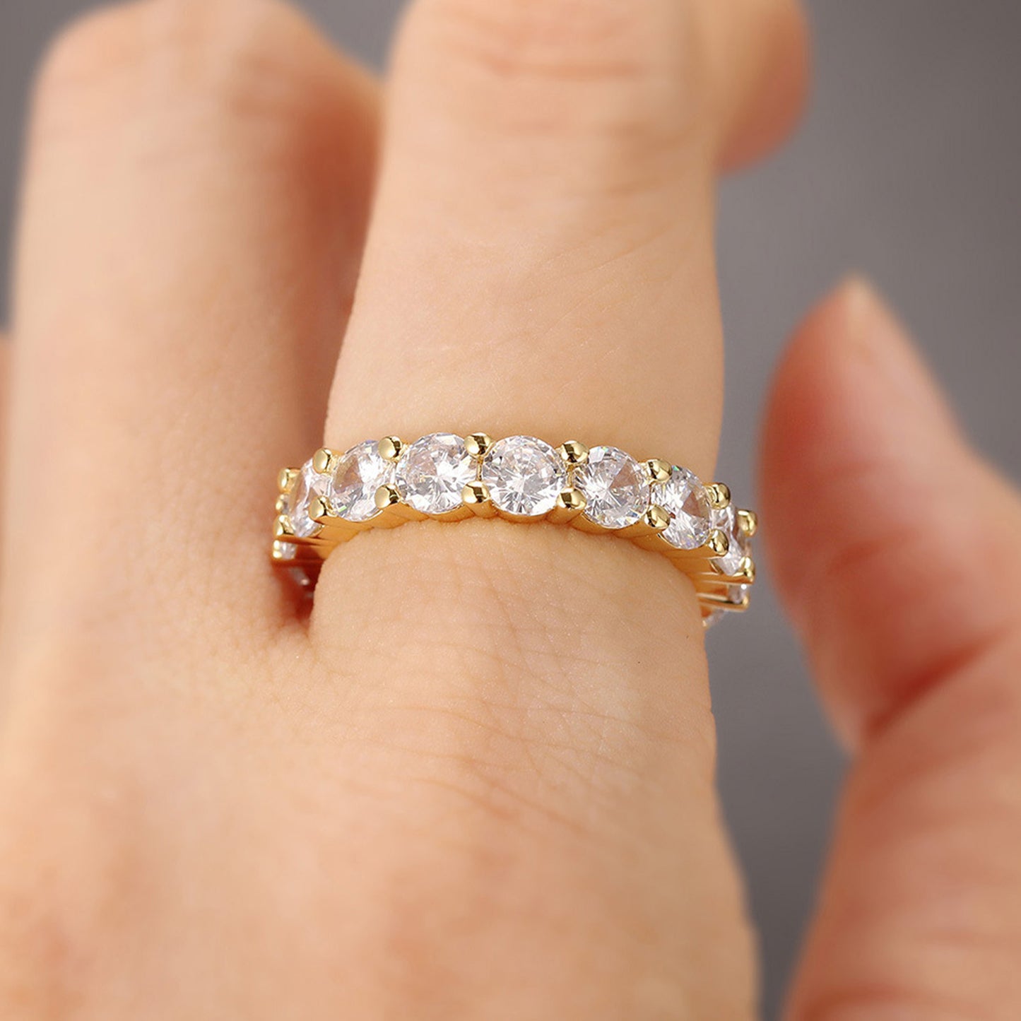 Gold ring with diamonds on a finger against a neutral background