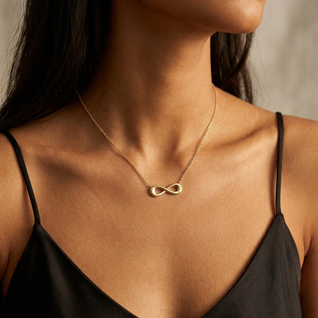 A close-up of a model wearing a delicate gold infinity necklace with a polished infinity symbol pendant, styled with a black spaghetti-strap camisole top.