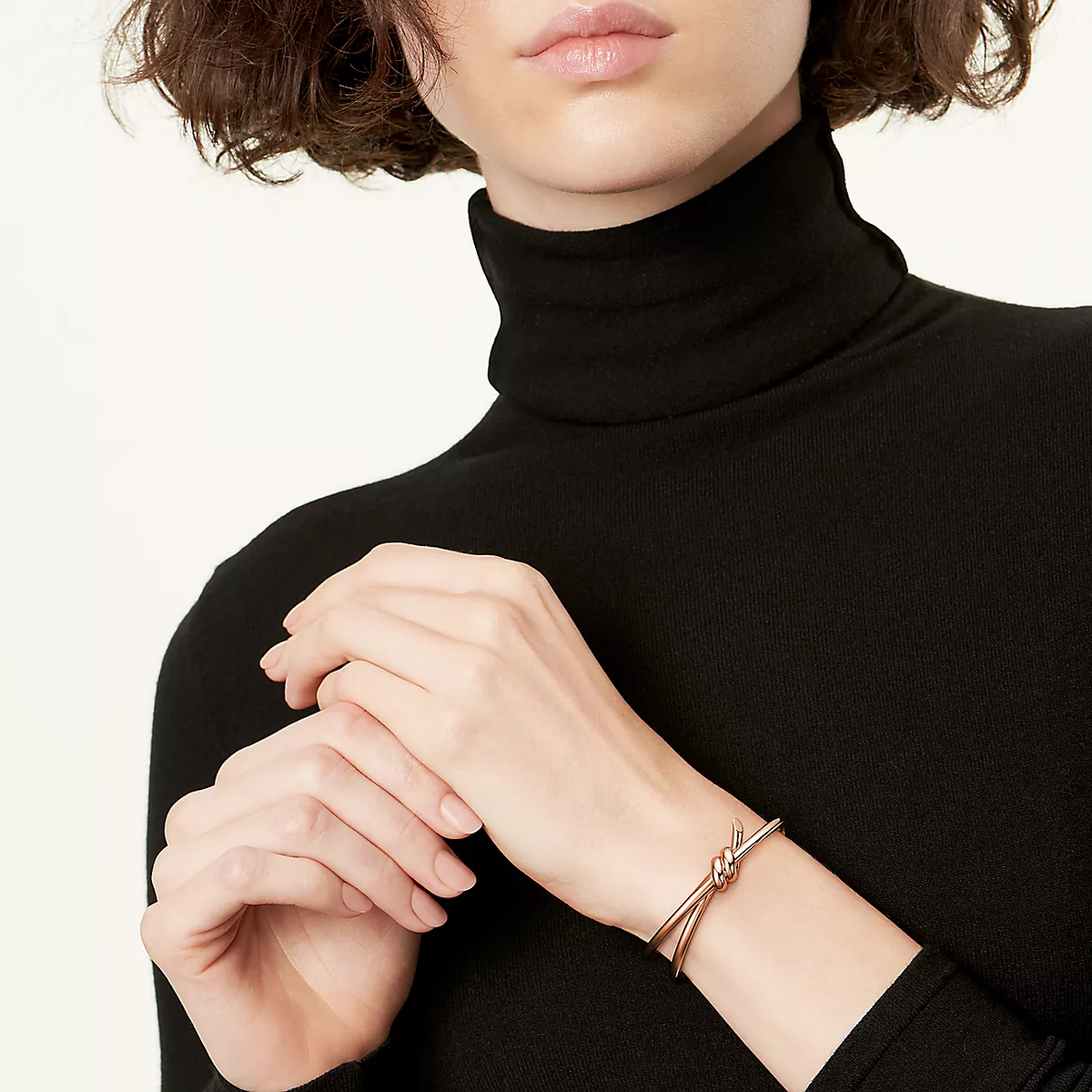 Person wearing a black turtleneck and a rose gold bracelet on a white background