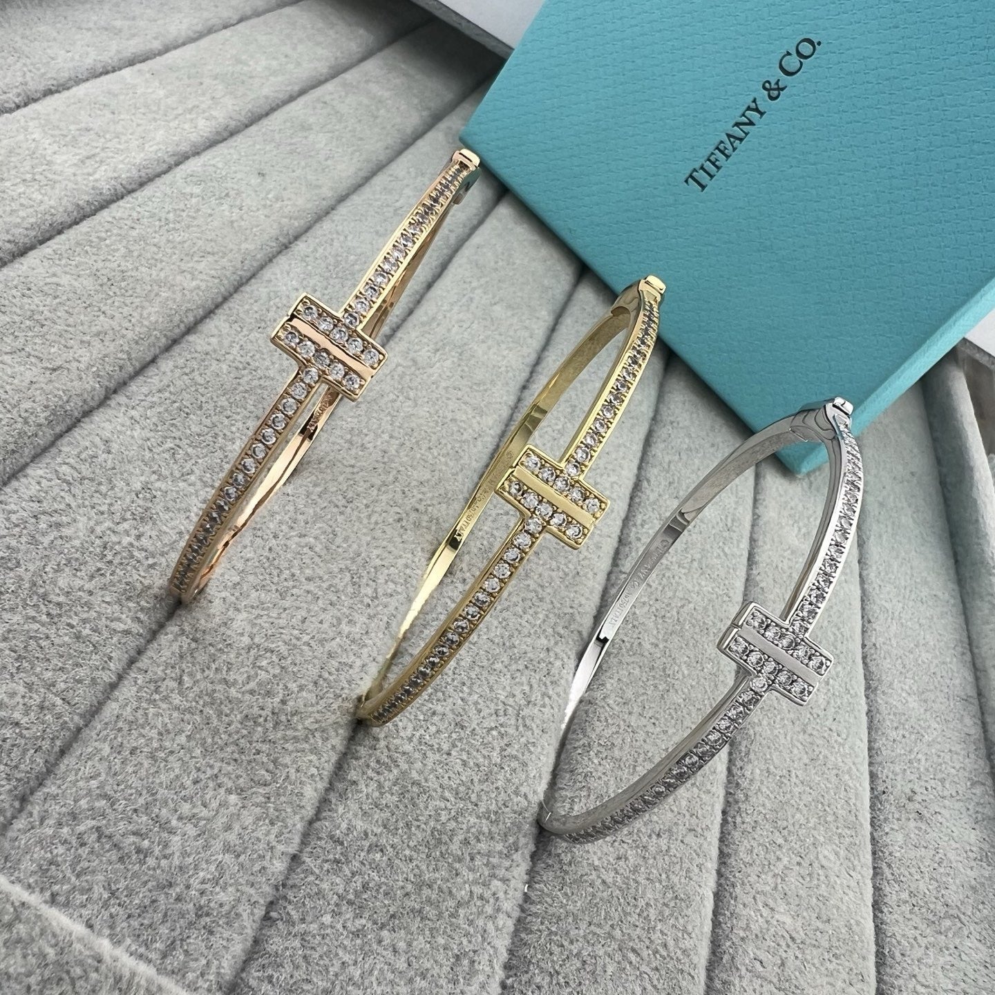 Two gold and silver bangles on a textured surface with a Tiffany & Co. box in the background.