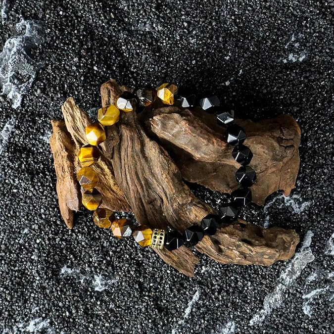 Three beaded bracelets on a piece of driftwood with a black sand background