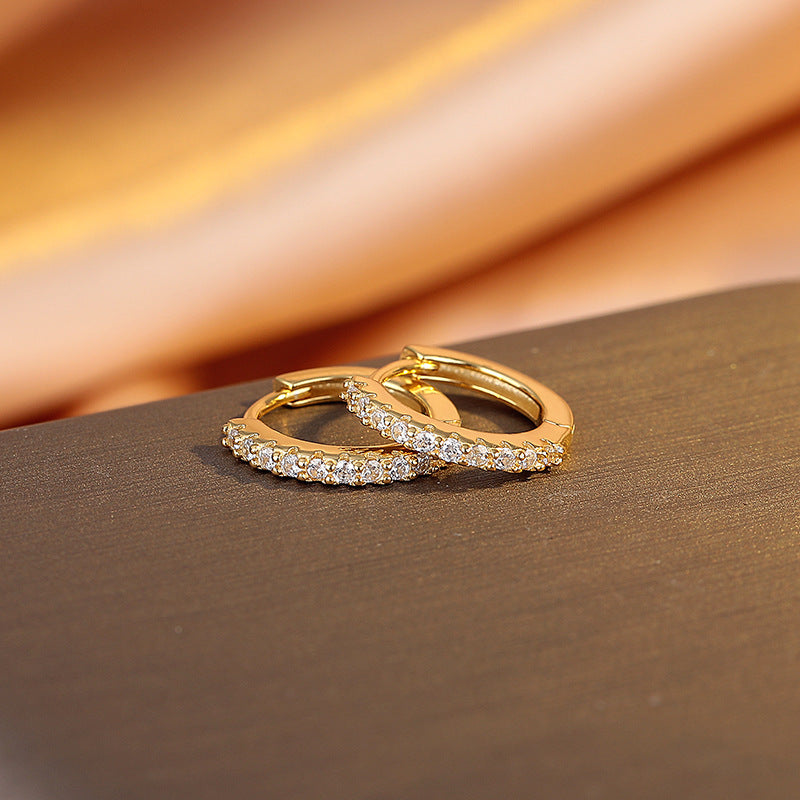 Pair of gold hoop earrings with embedded stones on a brown surface
