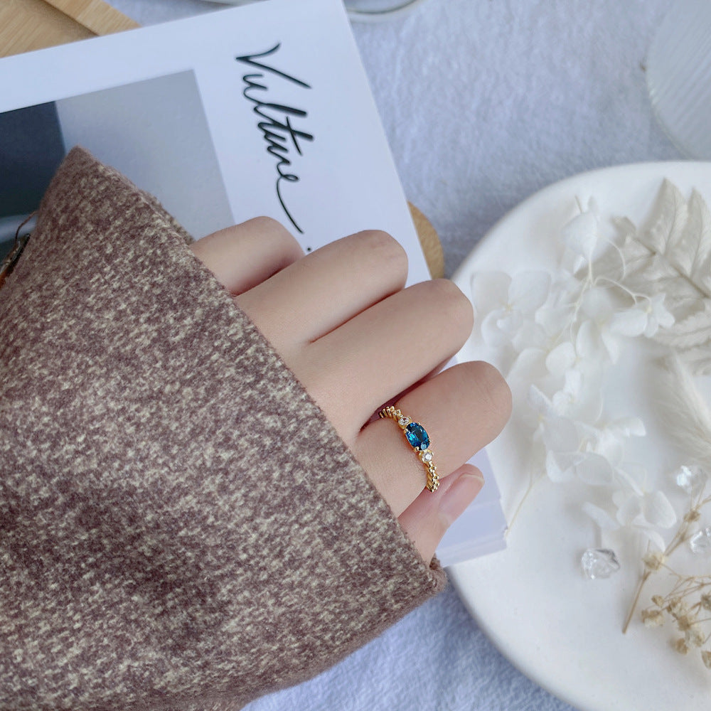 Hand wearing a gold ring with a blue gemstone on a textured surface