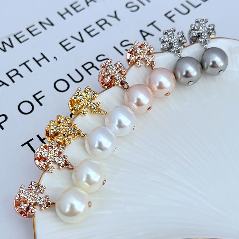 Macro view focusing on the engraved details of the Double T logo and the smooth, luminous surface of the pearl.