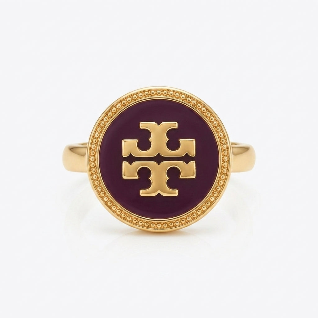 A gold signet ring featuring a circular dark purple enamel face with a raised gold monogram logo, set against a clean white background.