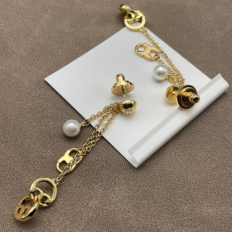 Both earrings displayed hanging freely against a dark, solid background, clearly showing the layered chains, pearls, and logo stud.