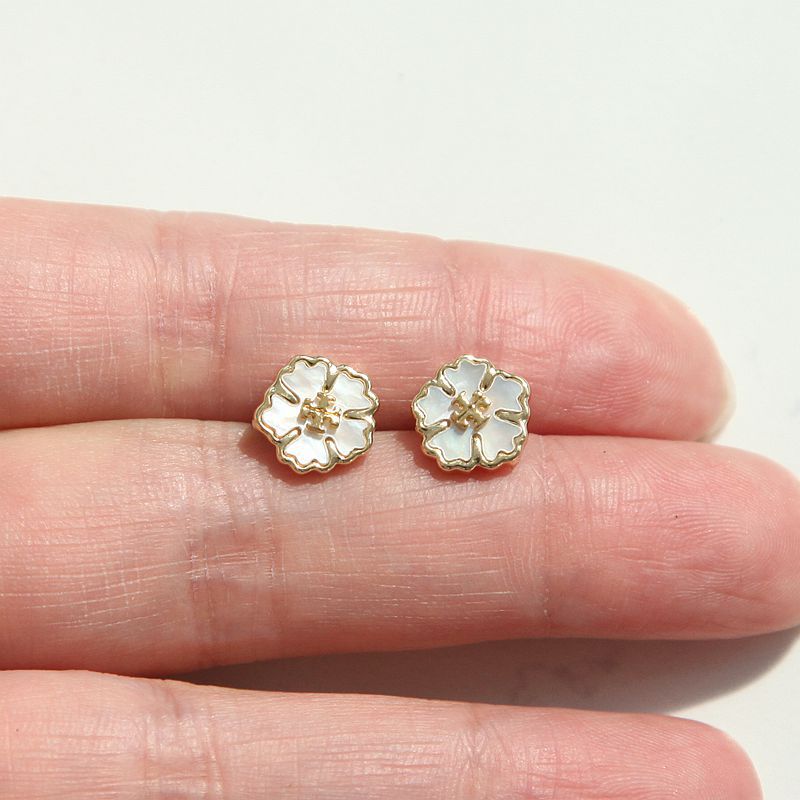 Flower-shaped earrings held between two fingers on a light background